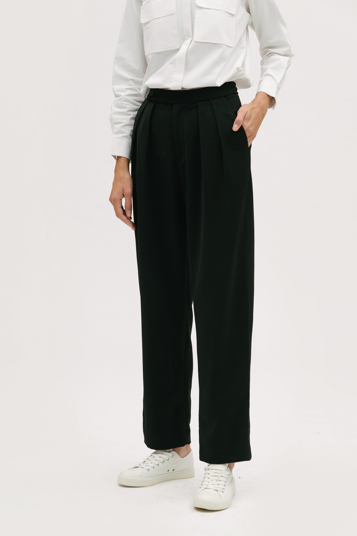 A woman wearing a white shirt, black trousers and white tennis shoes.