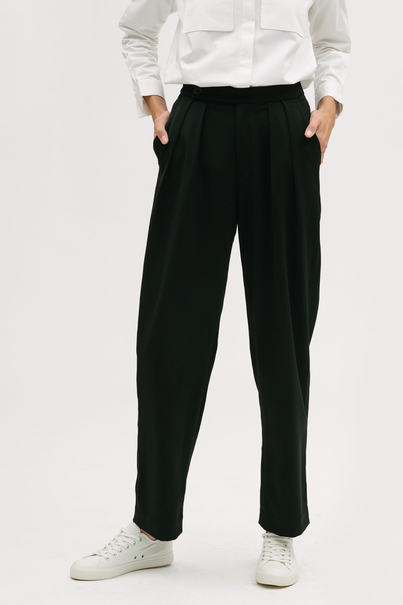 A woman wearing a white shirt, black trousers and white tennis shoes.
