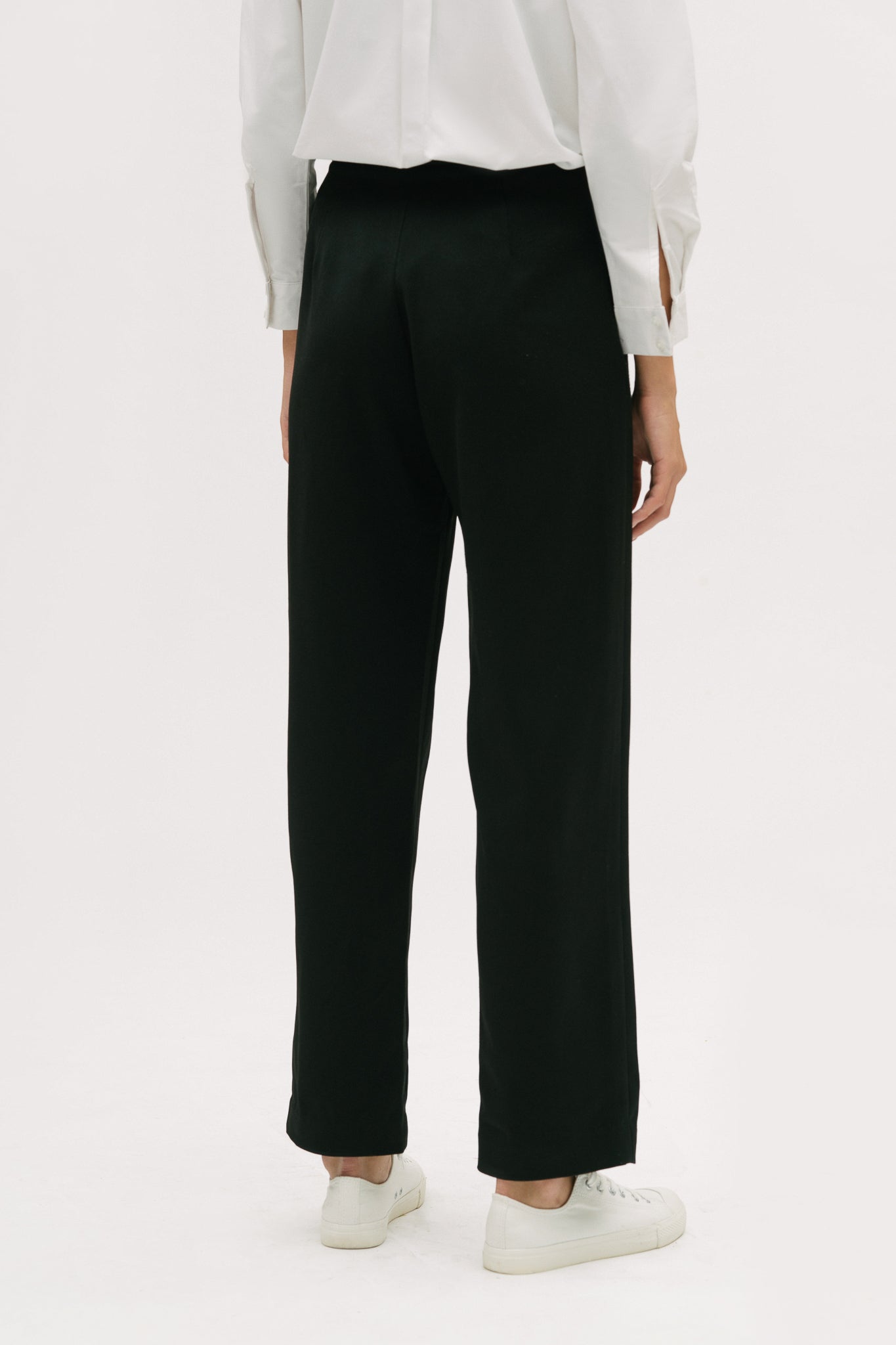 A woman wearing a white shirt, black trousers and white tennis shoes.