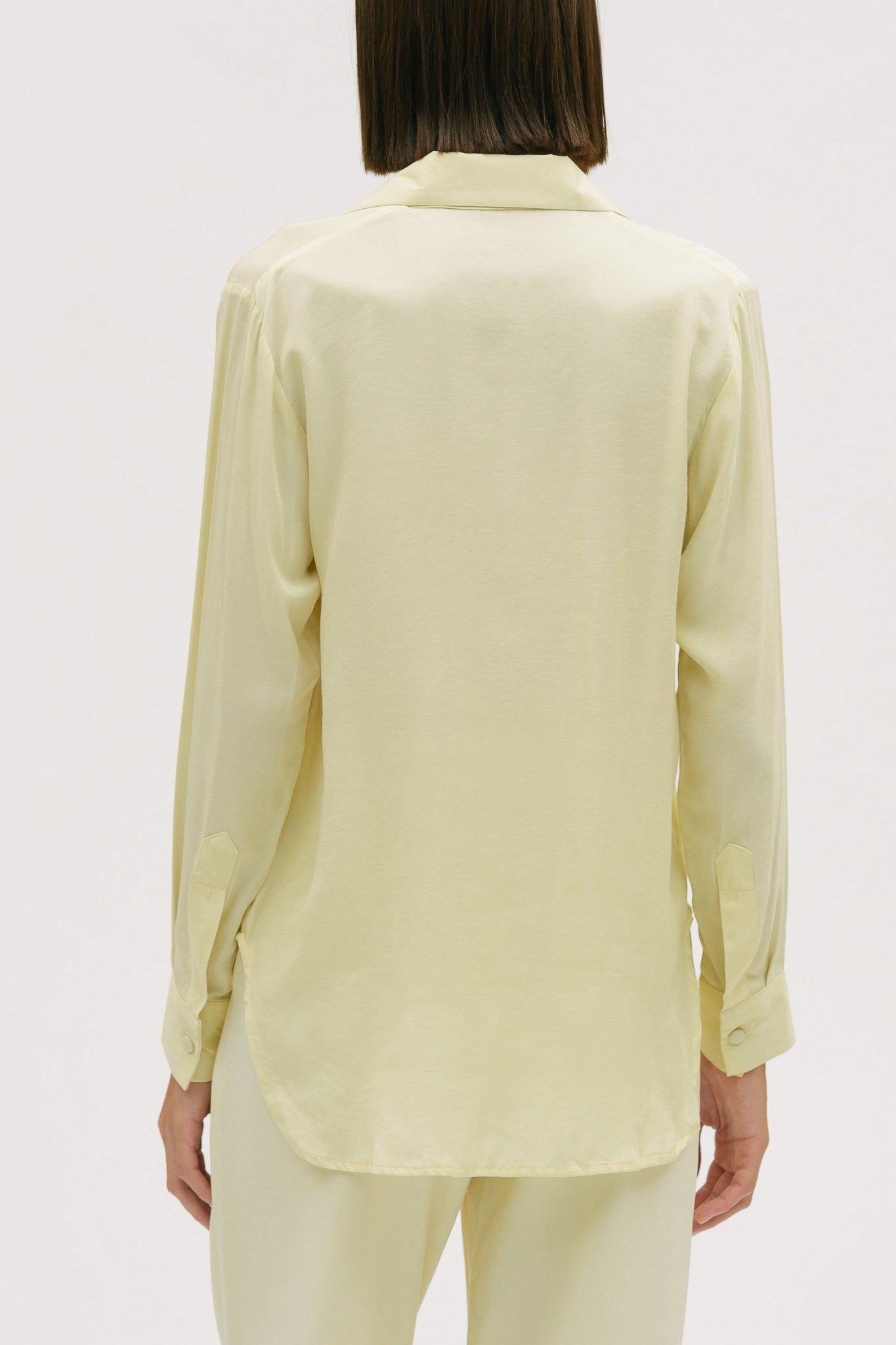 A woman is wearing a lightweight yellow shirt and trousers
