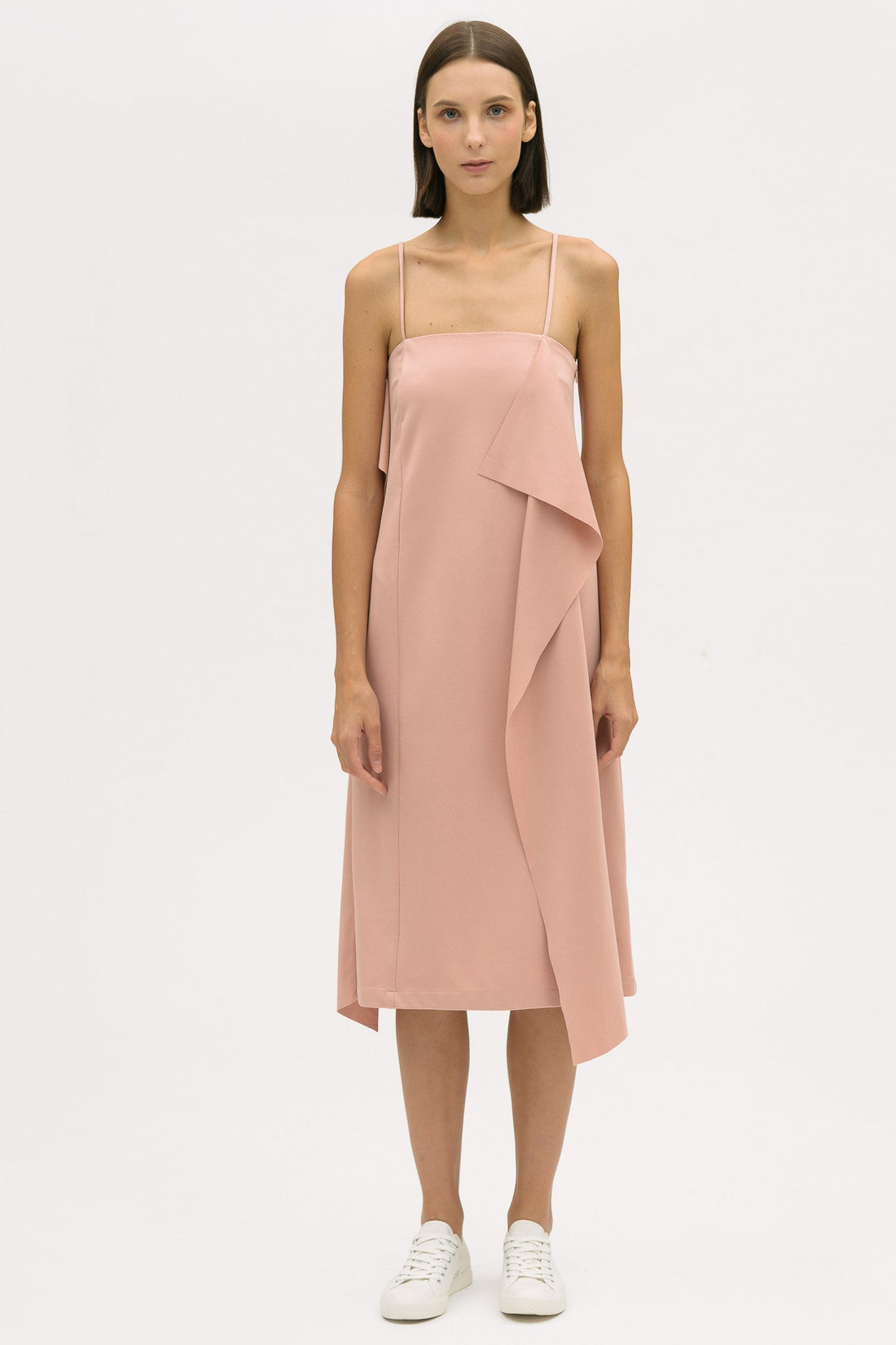A woman is wearing a pink slip dress with ruffles. She also has white tennis shoes on.
