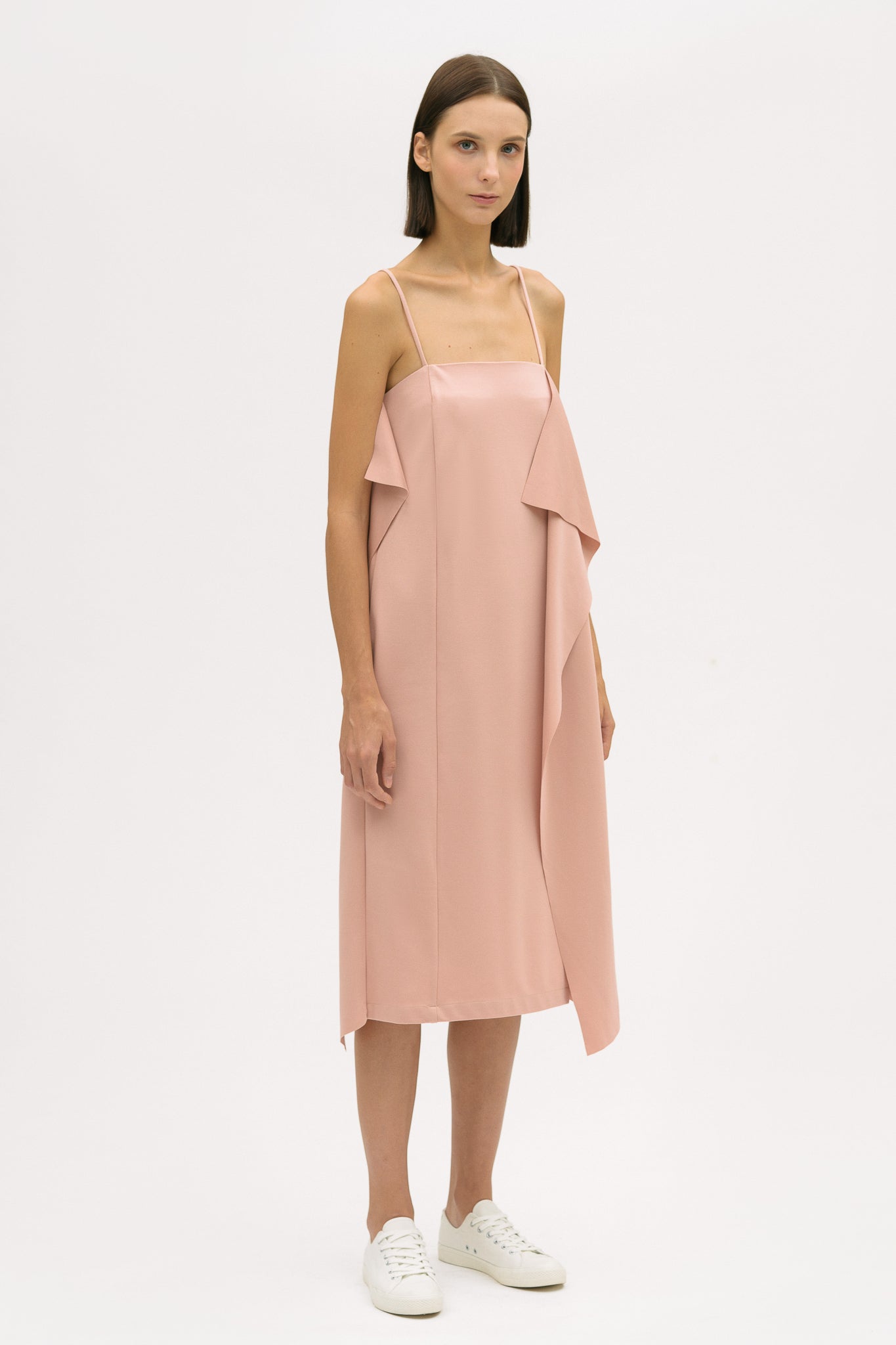 A woman is wearing a pink slip dress with ruffles. She also has white tennis shoes on.
