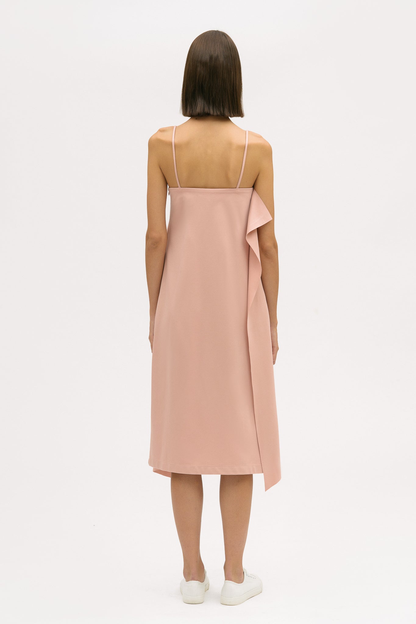 A woman is wearing a pink slip dress with ruffles. She also has white tennis shoes on.