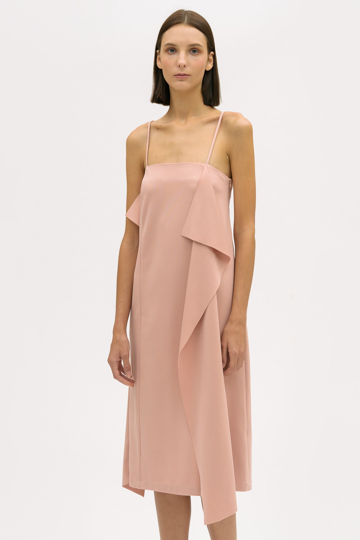 A woman is wearing a pink slip dress with ruffles. She also has white tennis shoes on.