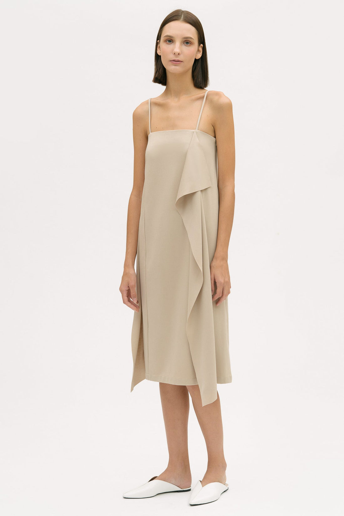 A woman is wearing a beige slip dress with ruffles. She also has white leather shoes on.