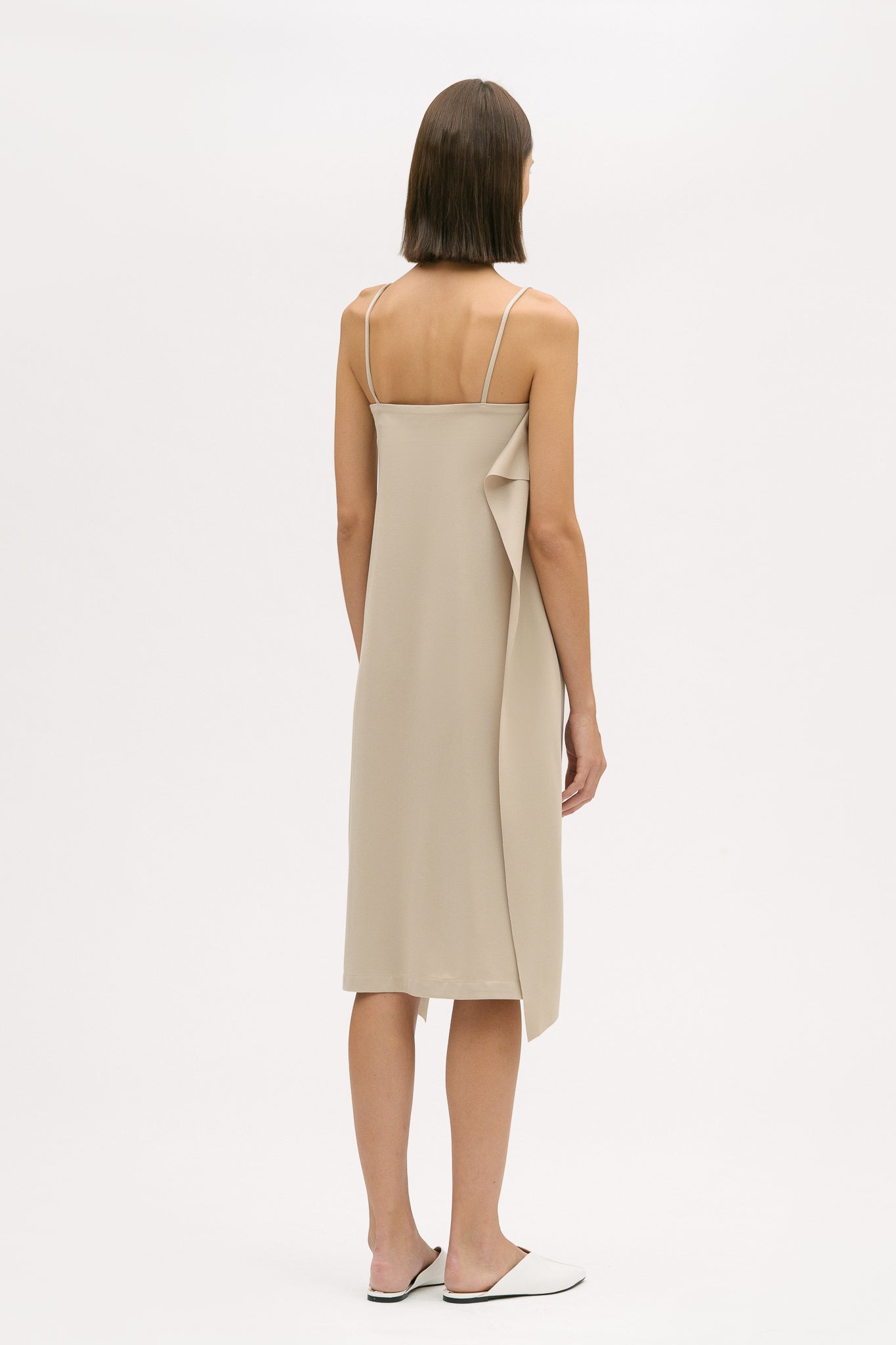 A woman is wearing a beige slip dress with ruffles. She also has white leather shoes on.