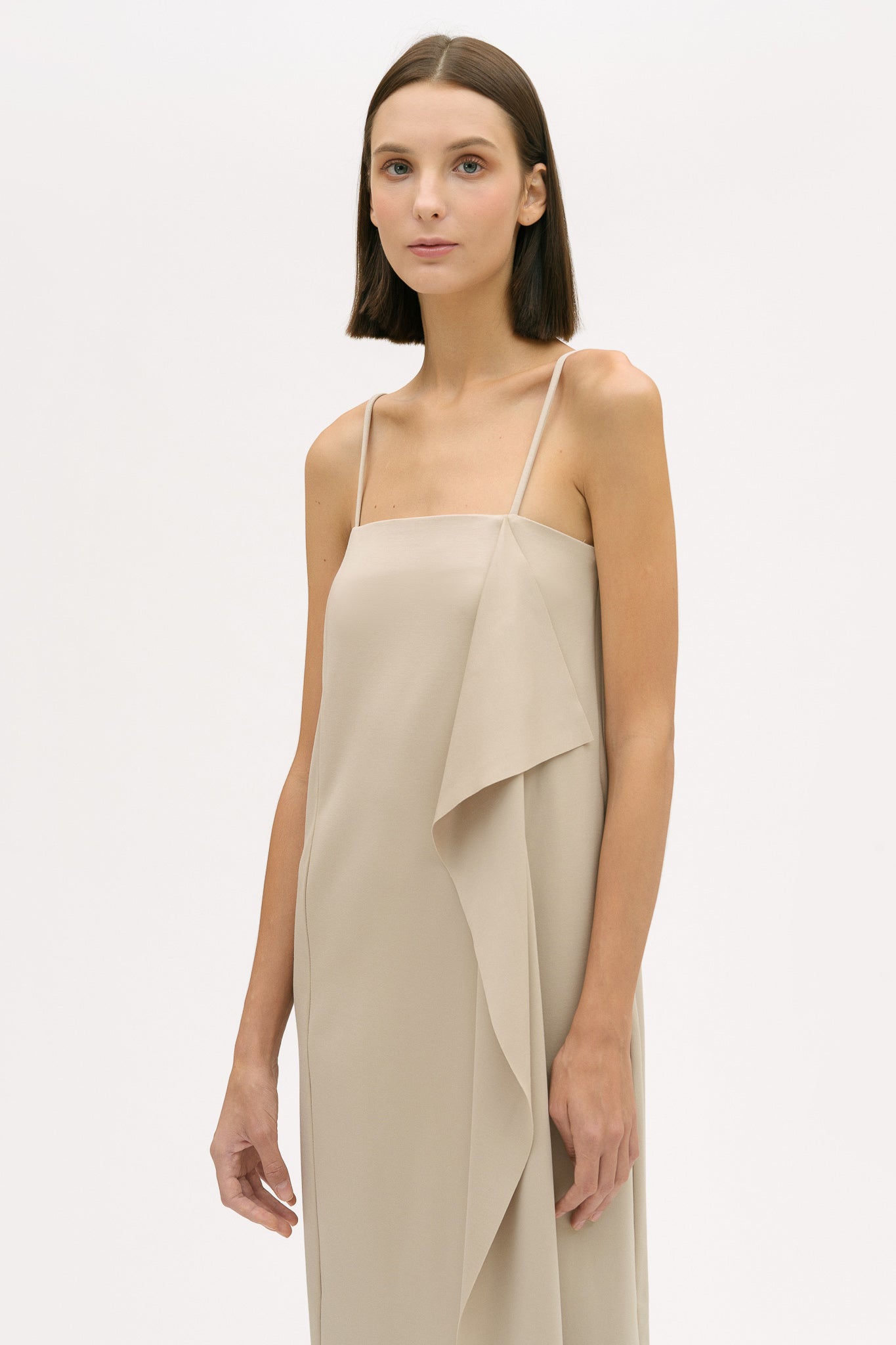A woman is wearing a beige slip dress with ruffles. She also has white leather shoes on.