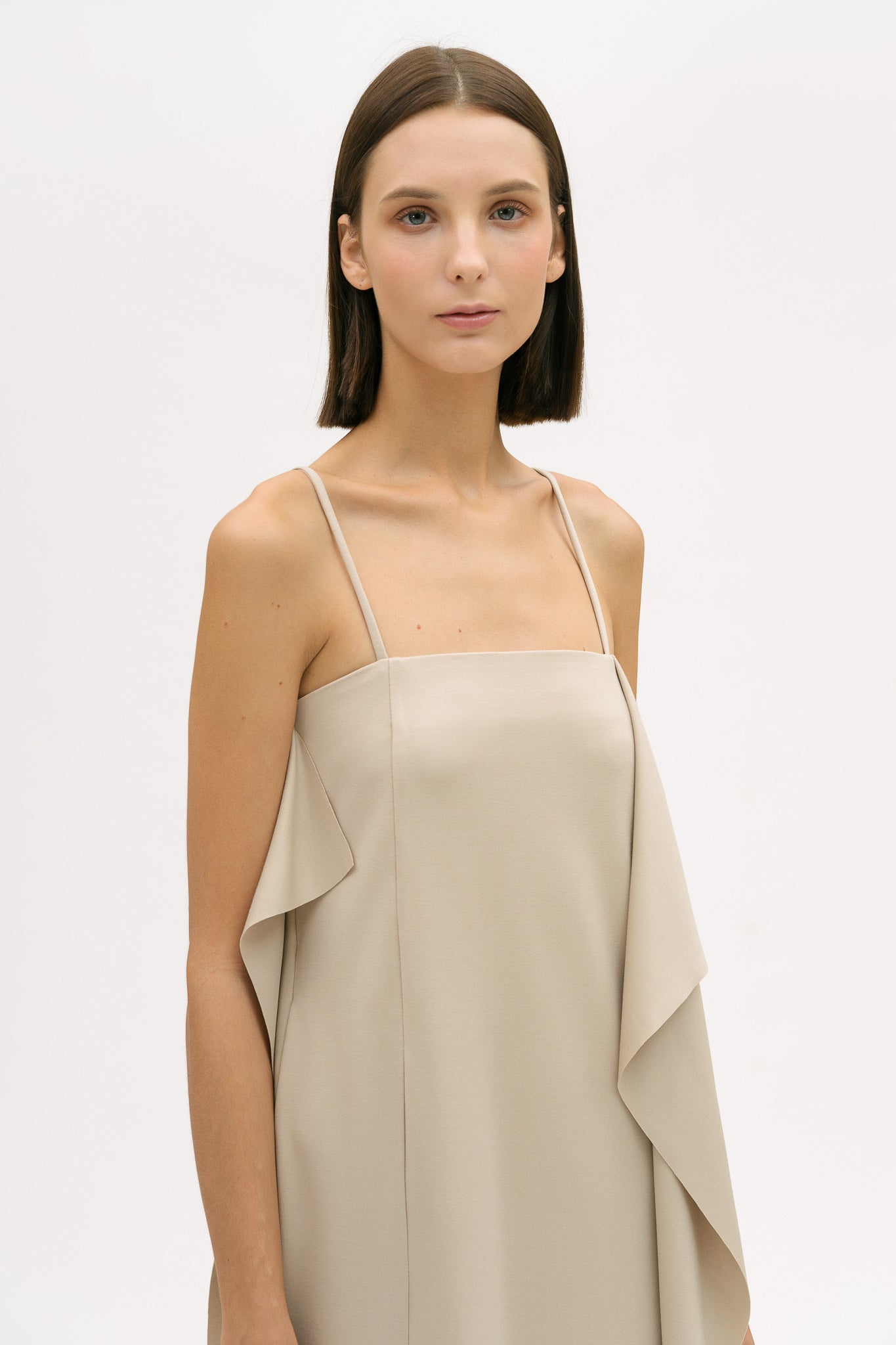 A woman is wearing a beige slip dress with ruffles.