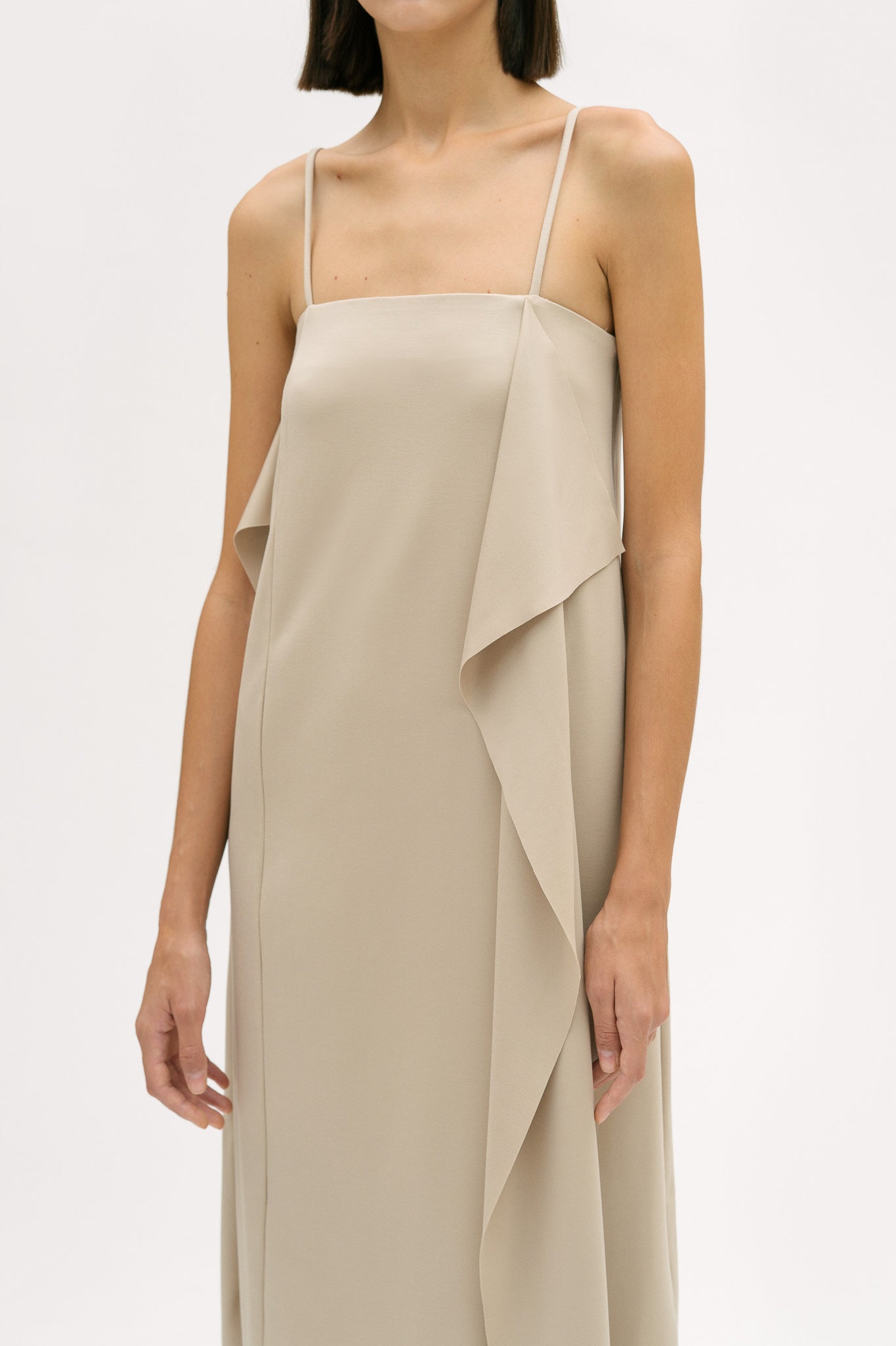 A woman is wearing a beige slip dress with ruffles.