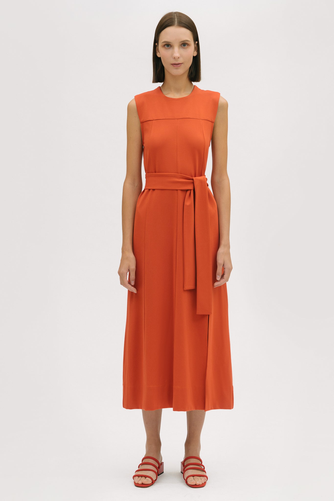 A woman wearing an orange dress.  She is also wearing red strappy sandals.