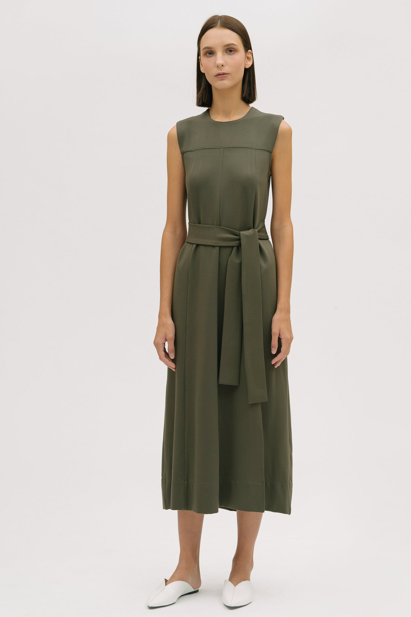 A woman wearing a dusty olive dress. She is also wearing white shoes.