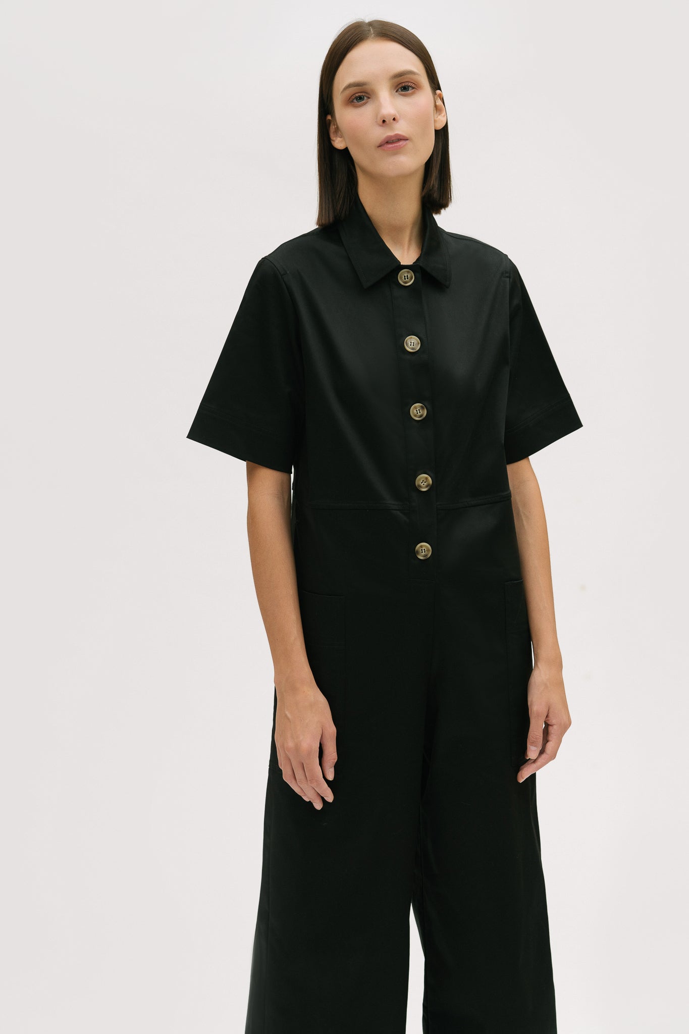 A woman with short brown hair is wearing a black collared jumpsuit.