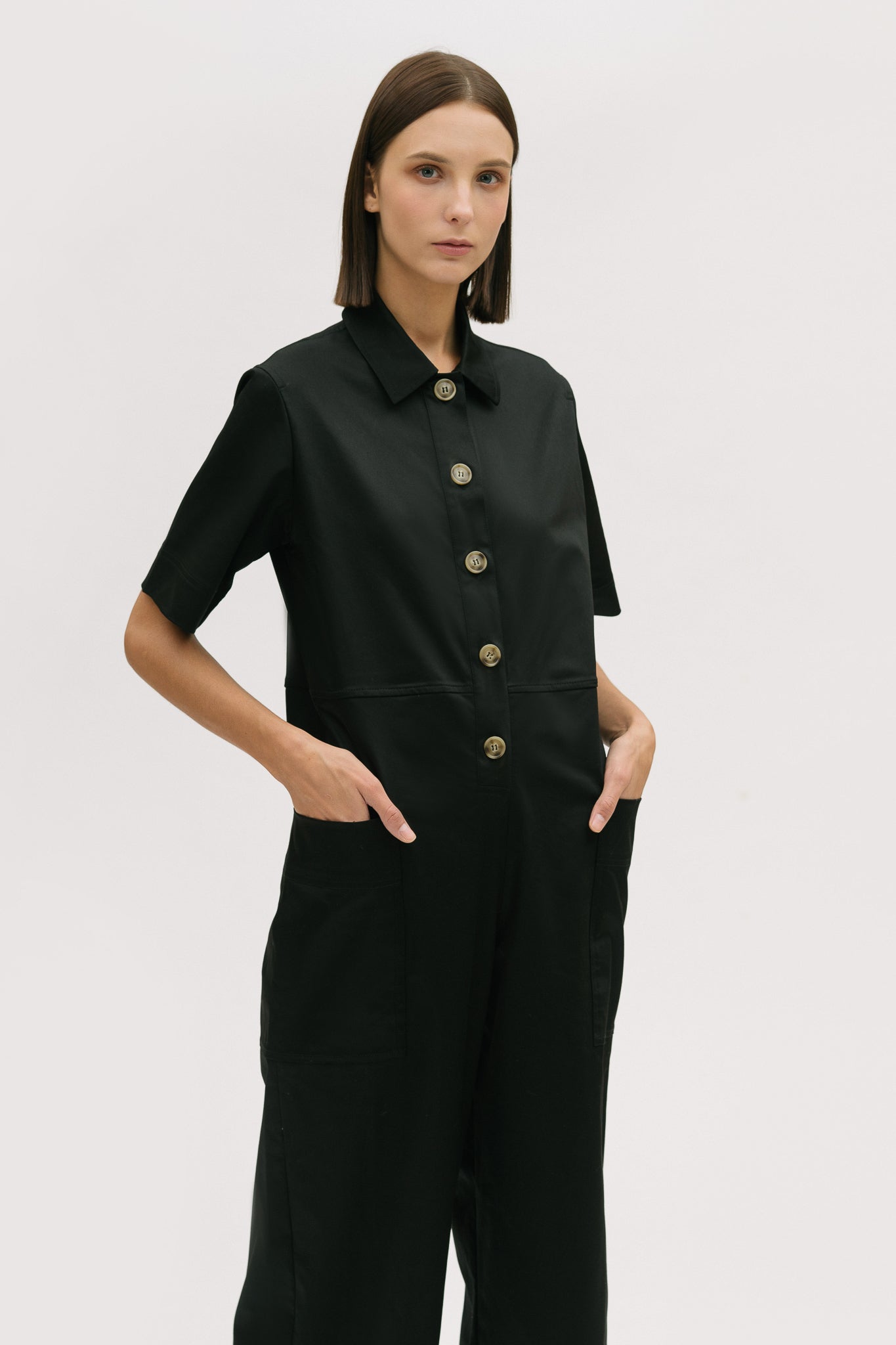 A woman with short brown hair is wearing a black collared jumpsuit.