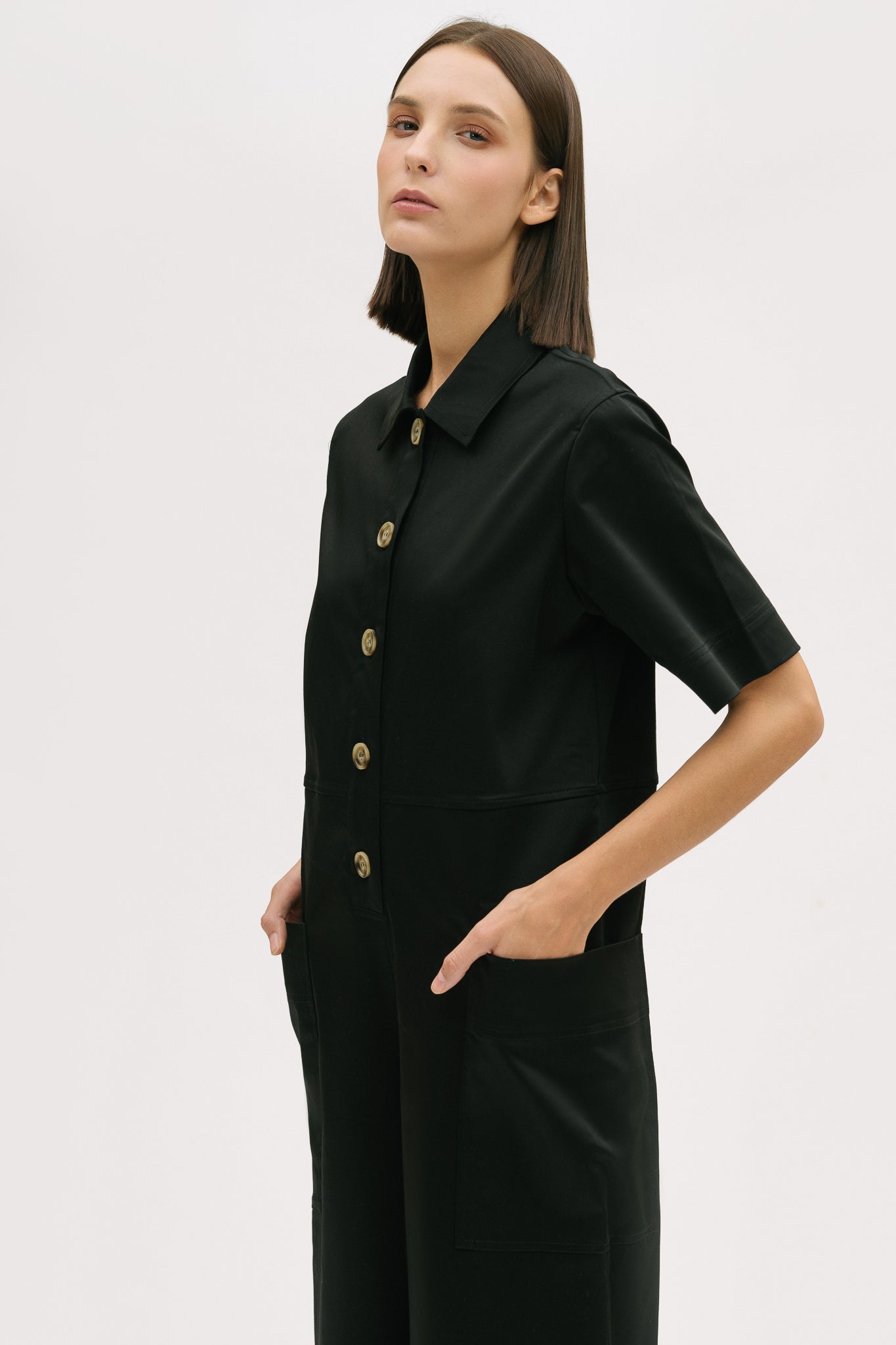 A woman with short brown hair is wearing a black collared jumpsuit.