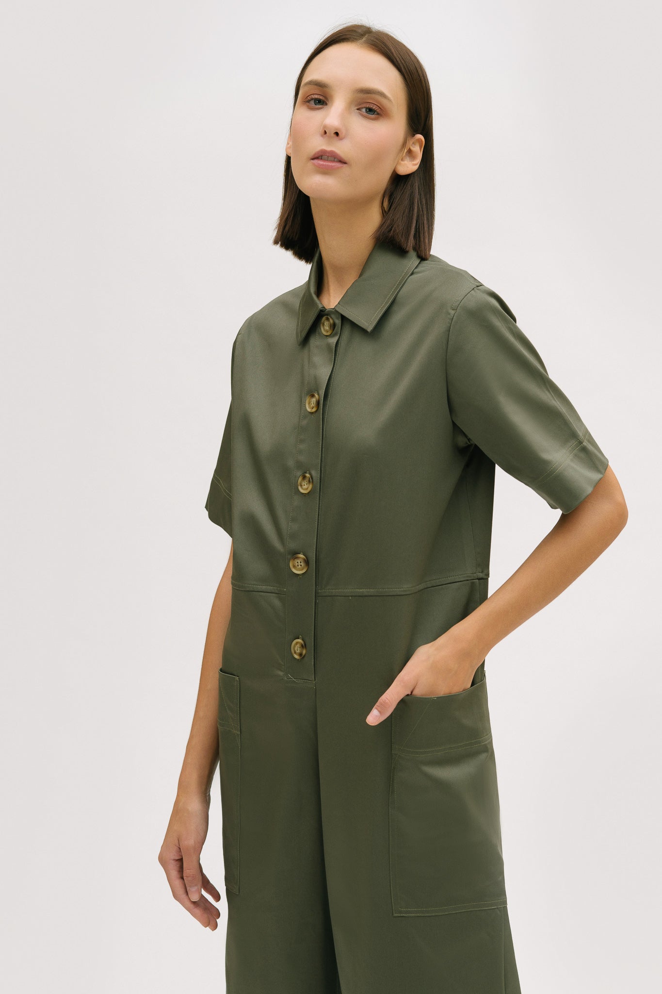 A woman with short brown hair is wearing a green collared jumpsuit.