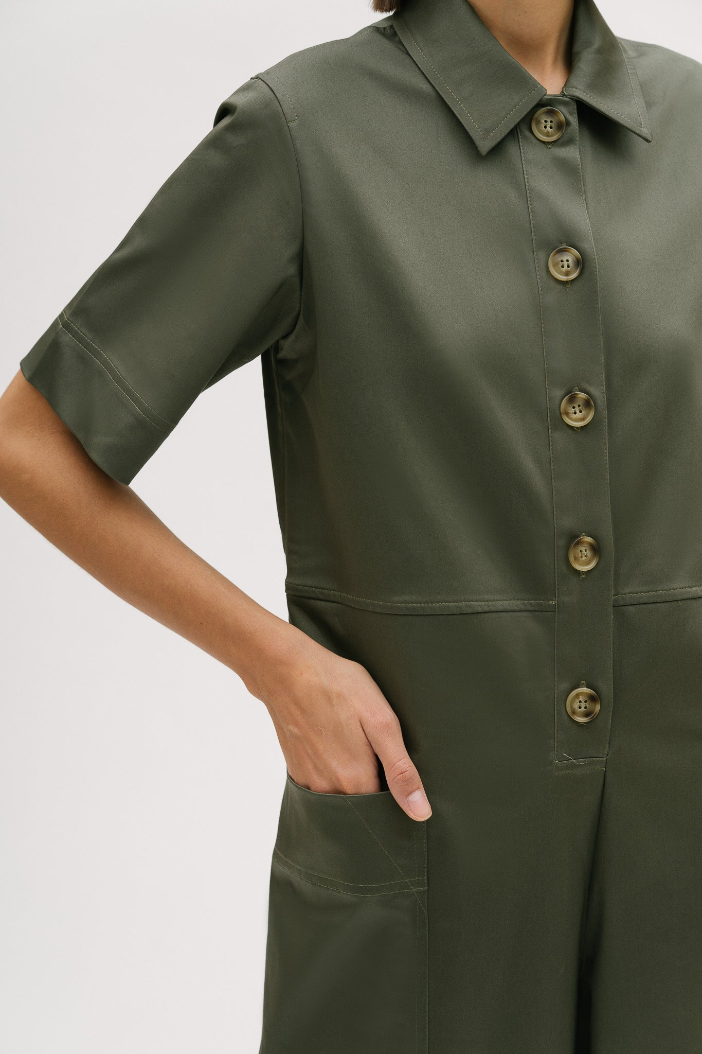A woman with short brown hair is wearing a green collared jumpsuit.
