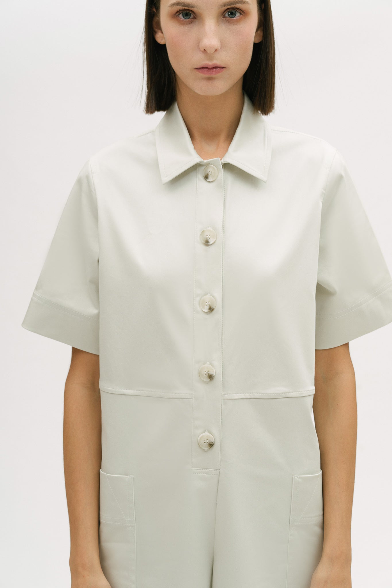 A woman with short brown hair is wearing a white collared jumpsuit