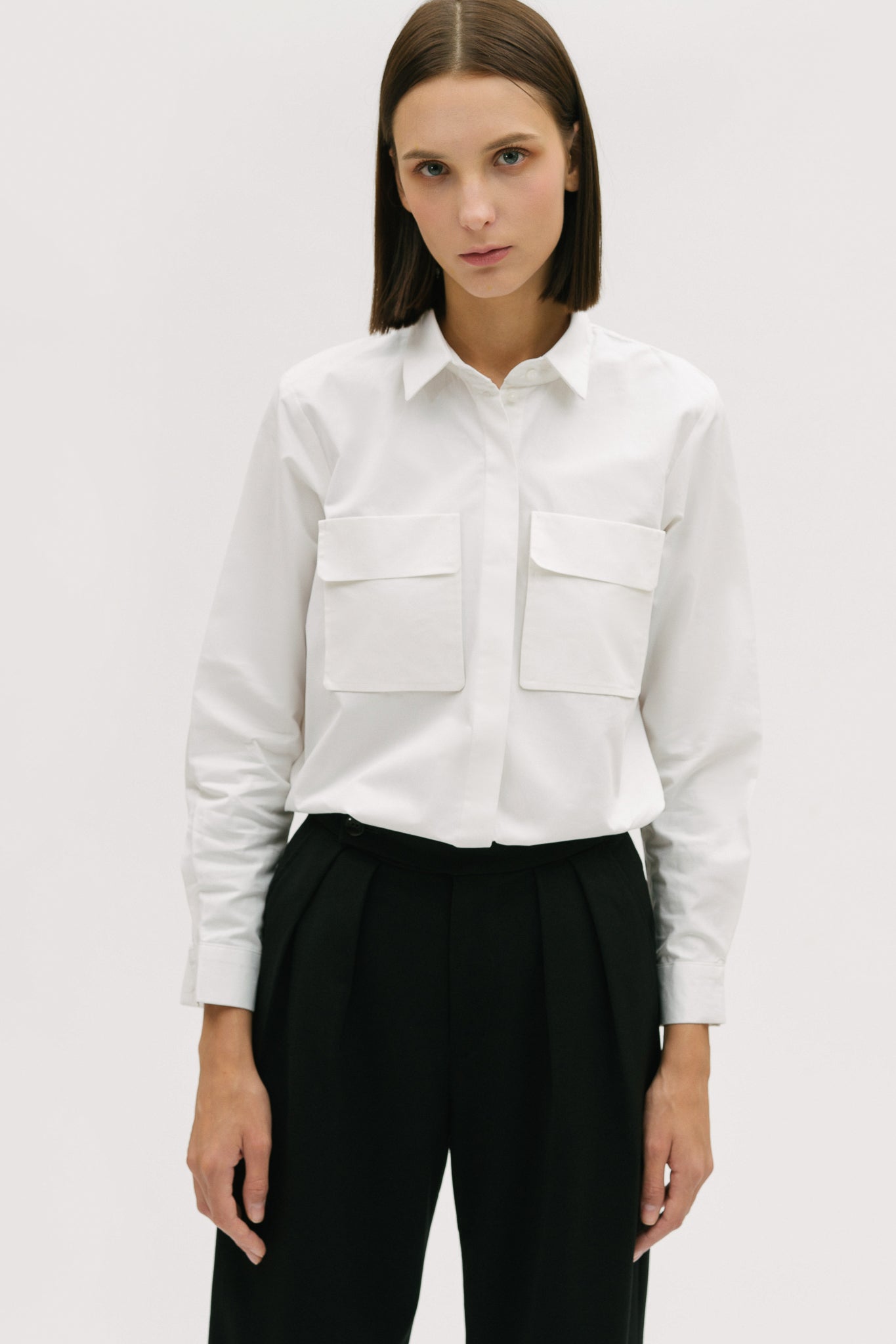 A woman wearing a white shirt, black trousers and white tennis shoes.