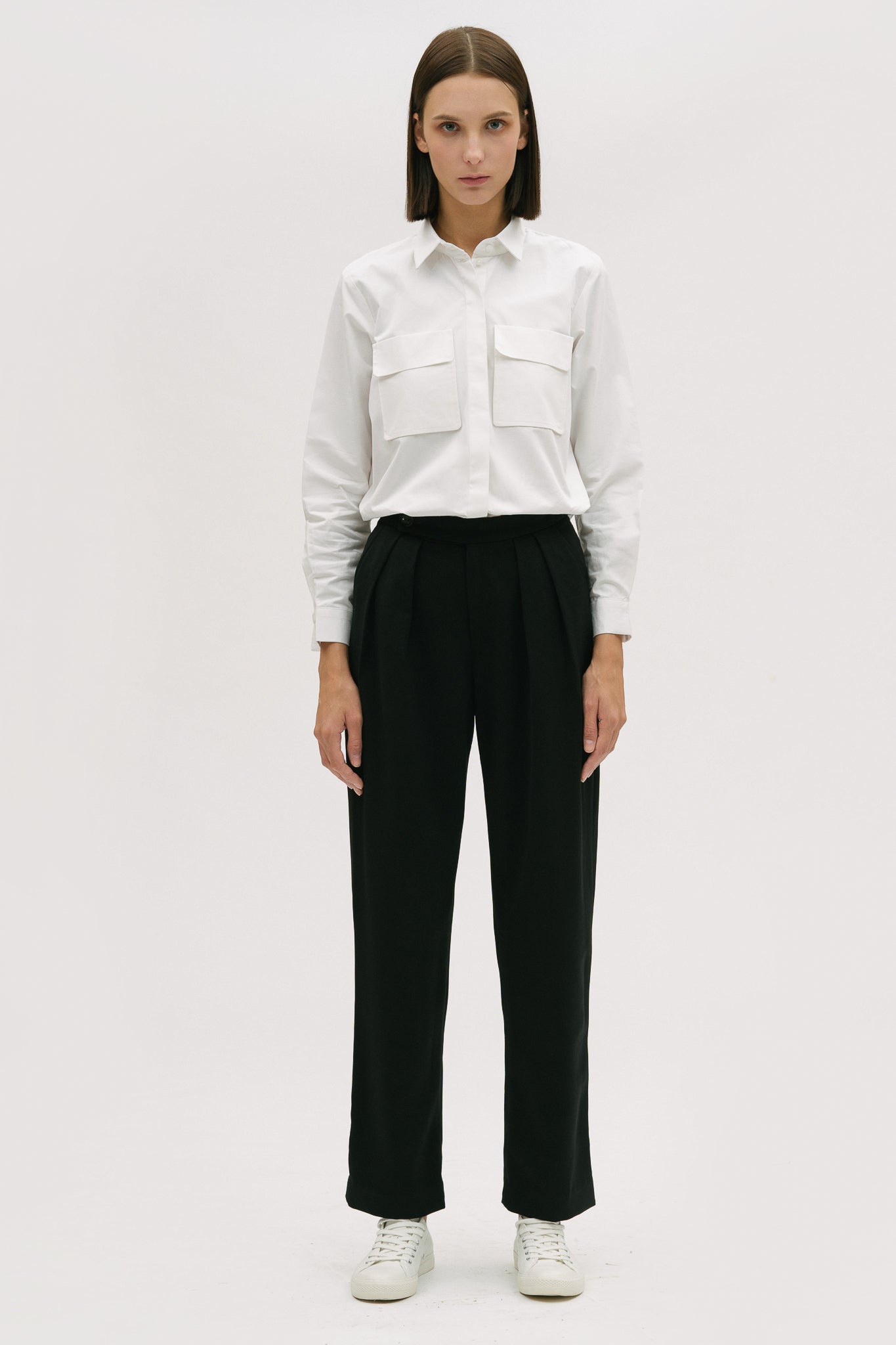 A woman wearing a white shirt, black trousers and white tennis shoes.