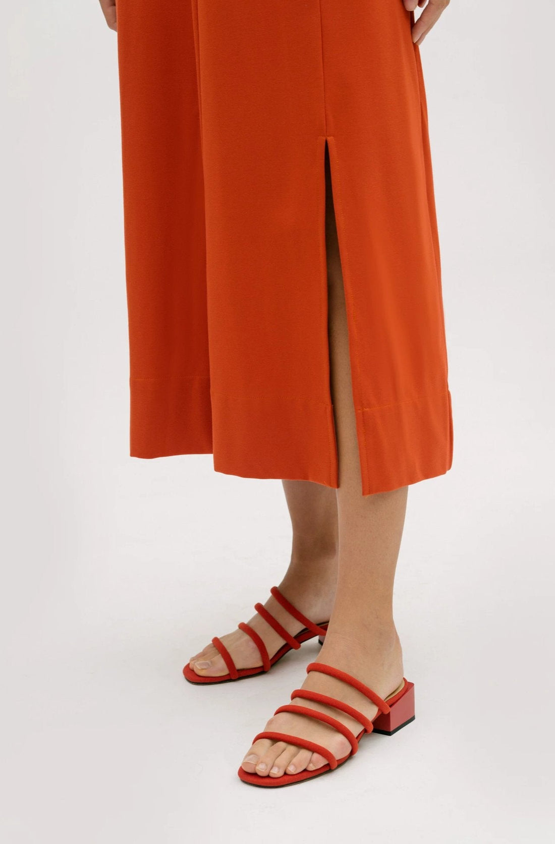 A woman wearing an orange dress.  She is also wearing red strappy sandals.