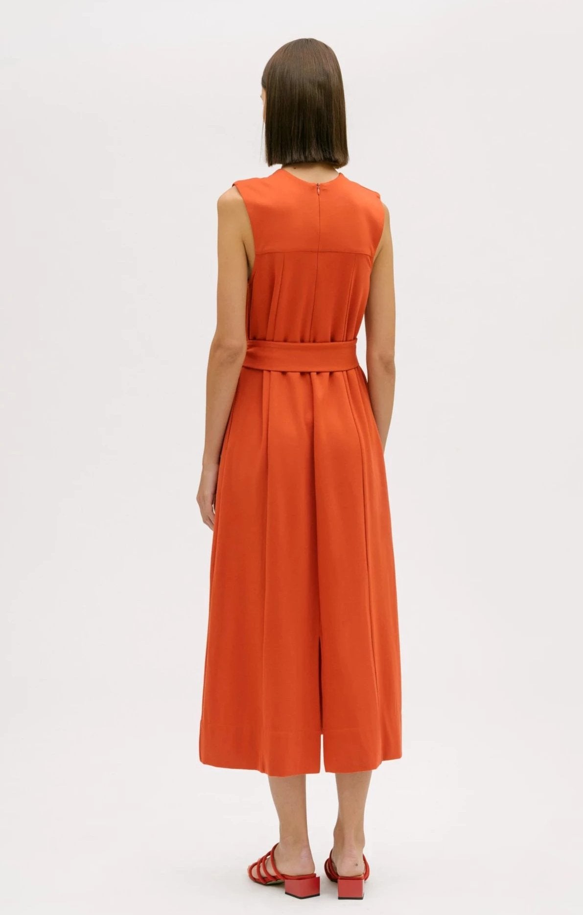A woman wearing an orange dress.  She is also wearing red strappy sandals.