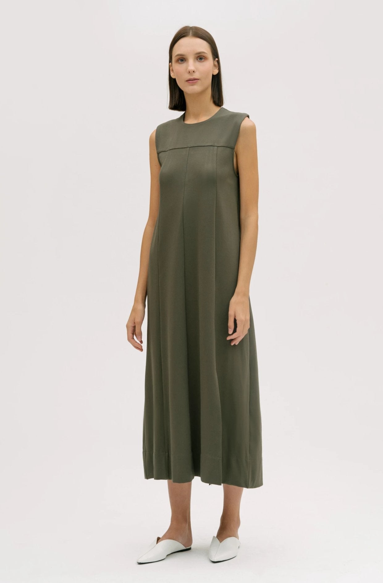 A woman wearing a dusty olive dress. She is also wearing white shoes.