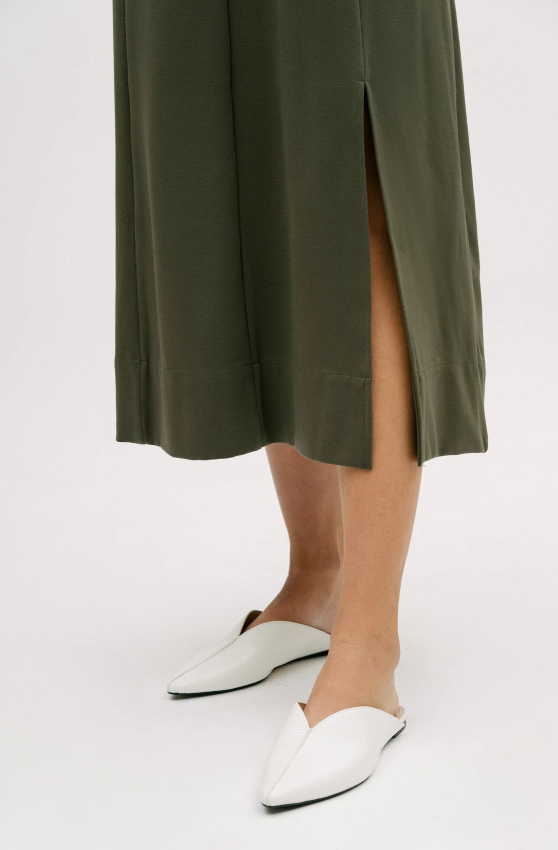 A woman wearing a dusty olive dress. She is also wearing white shoes.