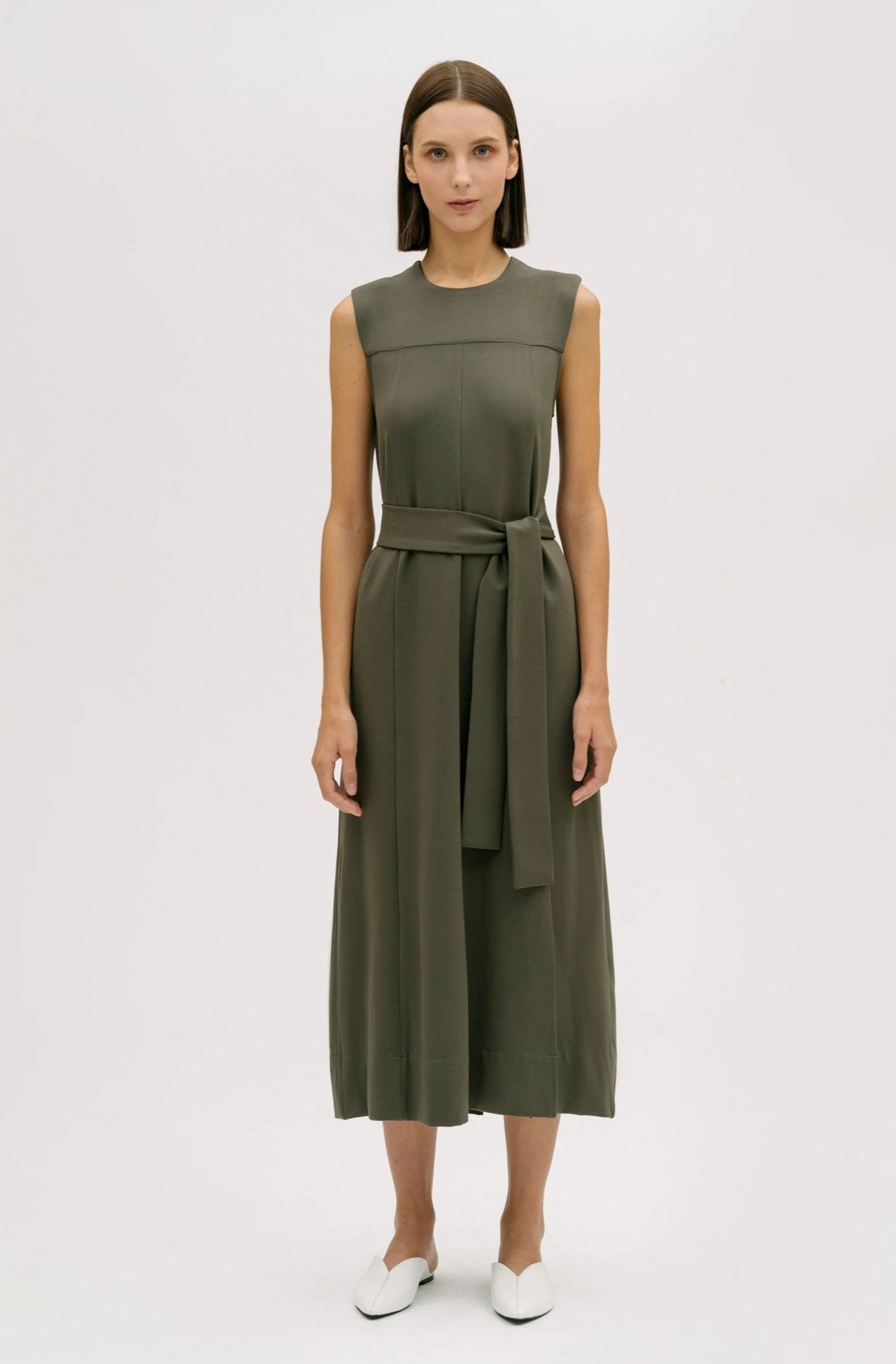 A woman wearing a dusty olive dress. She is also wearing white shoes.