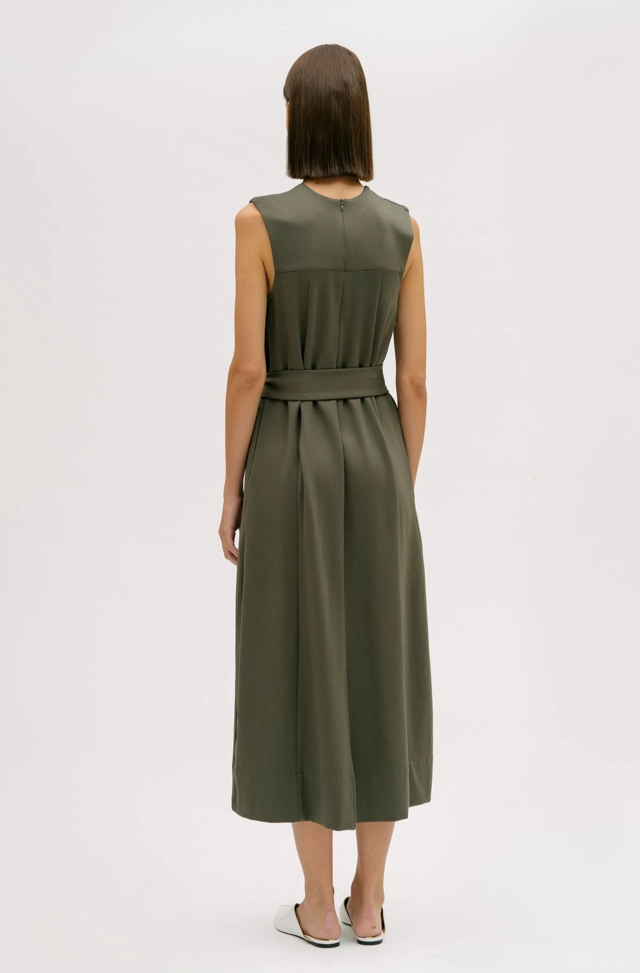 A woman wearing a dusty olive dress. She is also wearing white shoes.